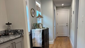 A hallway with wooden flooring, a kitchen area with a granite countertop, and a door at the end.