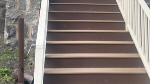 A set of wooden stairs leading to a front door with a stone pillar on the left.