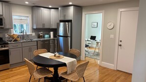 A modern kitchen with grey cabinets, a stainless steel refrigerator, and a dining area with a round table and wicker chairs.