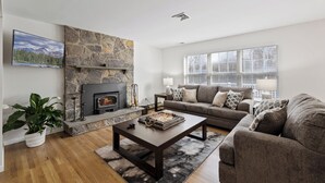 A modern living room with a stone fireplace, a large window, and a grey sofa. - Private 5-Bed Country Estate on 22 Acres (Chester)