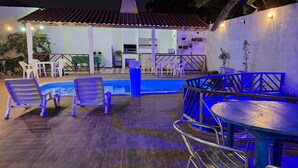 An outdoor pool area with lounge chairs and a dining table, surrounded by a white wall and a covered patio area. - Pousada Felix (São Gabriel)
