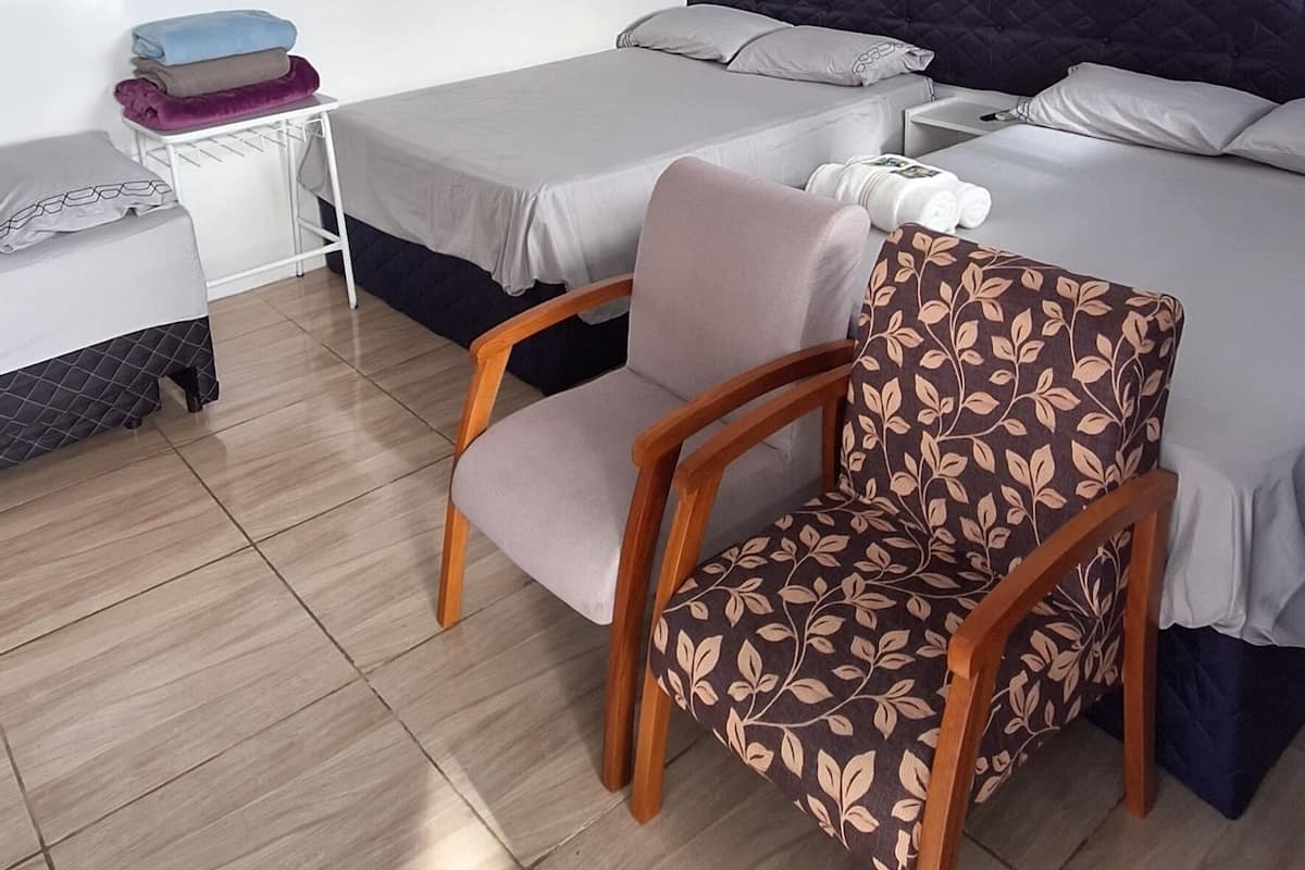 A hotel room with two beds, a chair, a bedside table, and a ceiling light.