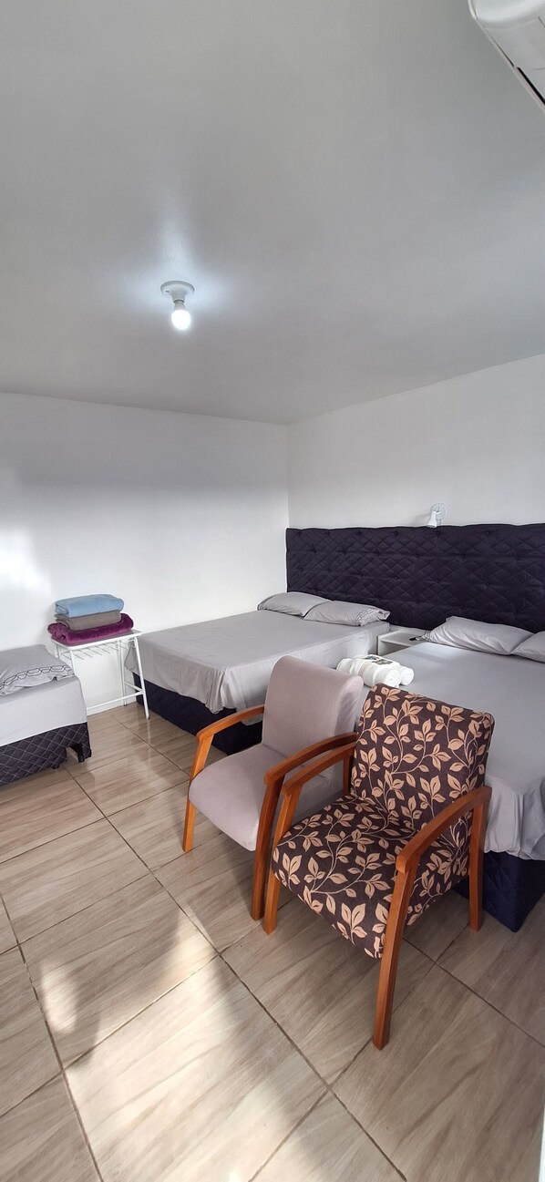 Habitación de hotel con dos camas, una silla, una mesita de noche y una lámpara en el techo.