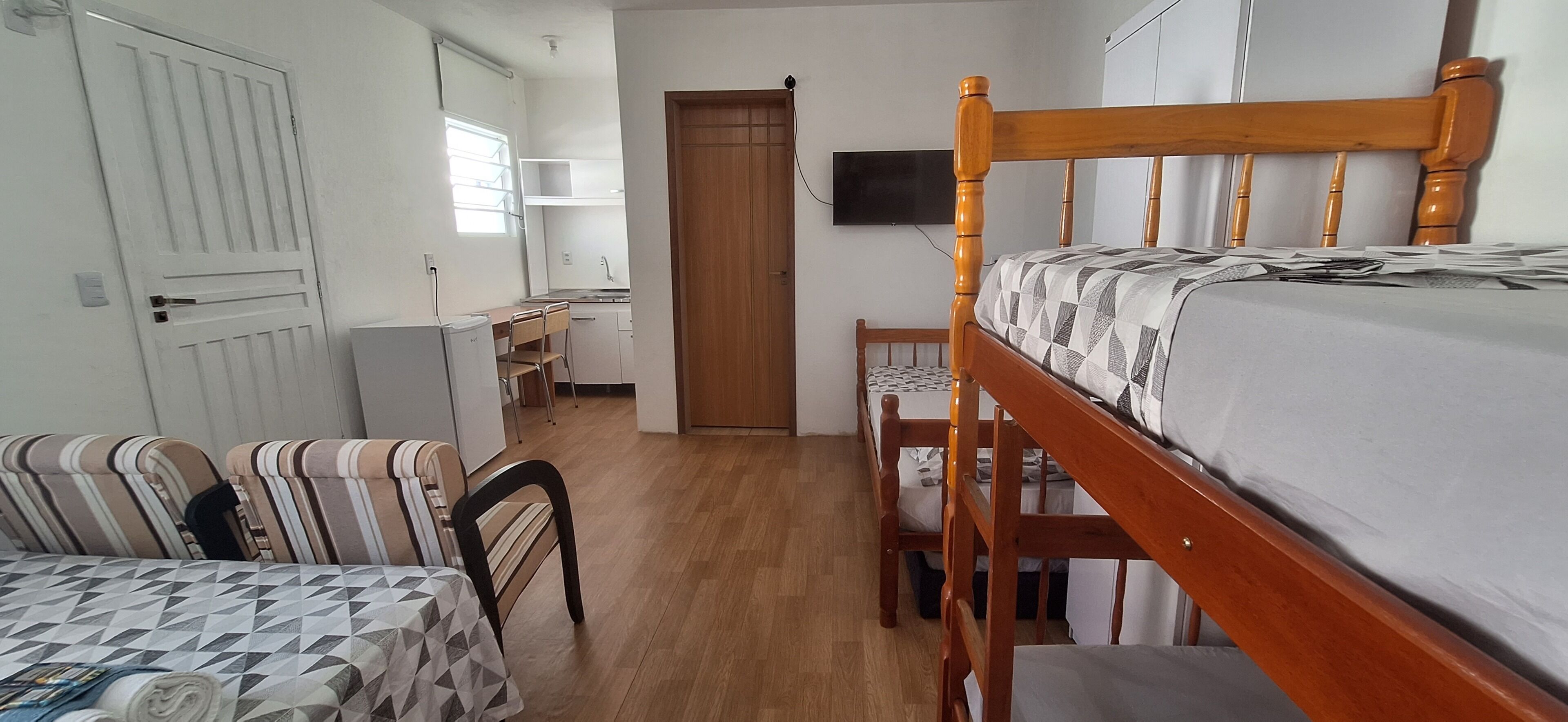 Una habitación compacta con una litera, un escritorio con silla, una kitchenette pequeña y un televisor montado en la pared.