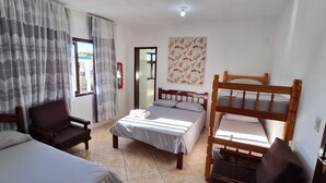 A room with two beds, a wooden bunk bed, a chair, a window with curtains, and a wall with a floral pattern. - Pousada Felix (São Gabriel)