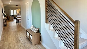 A modern interior with a wooden staircase, a bench, and a hallway leading to a living area. - Spacious 4BR Family Retreat- Comfort & Fun for All Ages (Shenandoah)