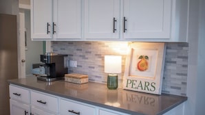 A kitchen with white cabinets, a coffee maker, a green vase, and a framed picture of a pear with the word "PEARS" on the counter. - Spacious 4BR Family Retreat- Comfort & Fun for All Ages (Shenandoah)