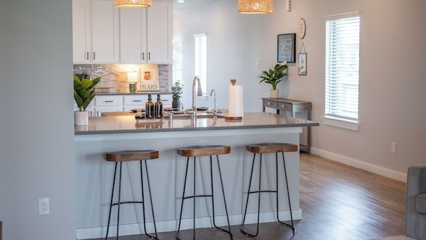 A modern kitchen with white cabinets, a central island with stools, pendant lighting, and a window with blinds. - Spacious 4BR Family Retreat- Comfort & Fun for All Ages (Shenandoah)
