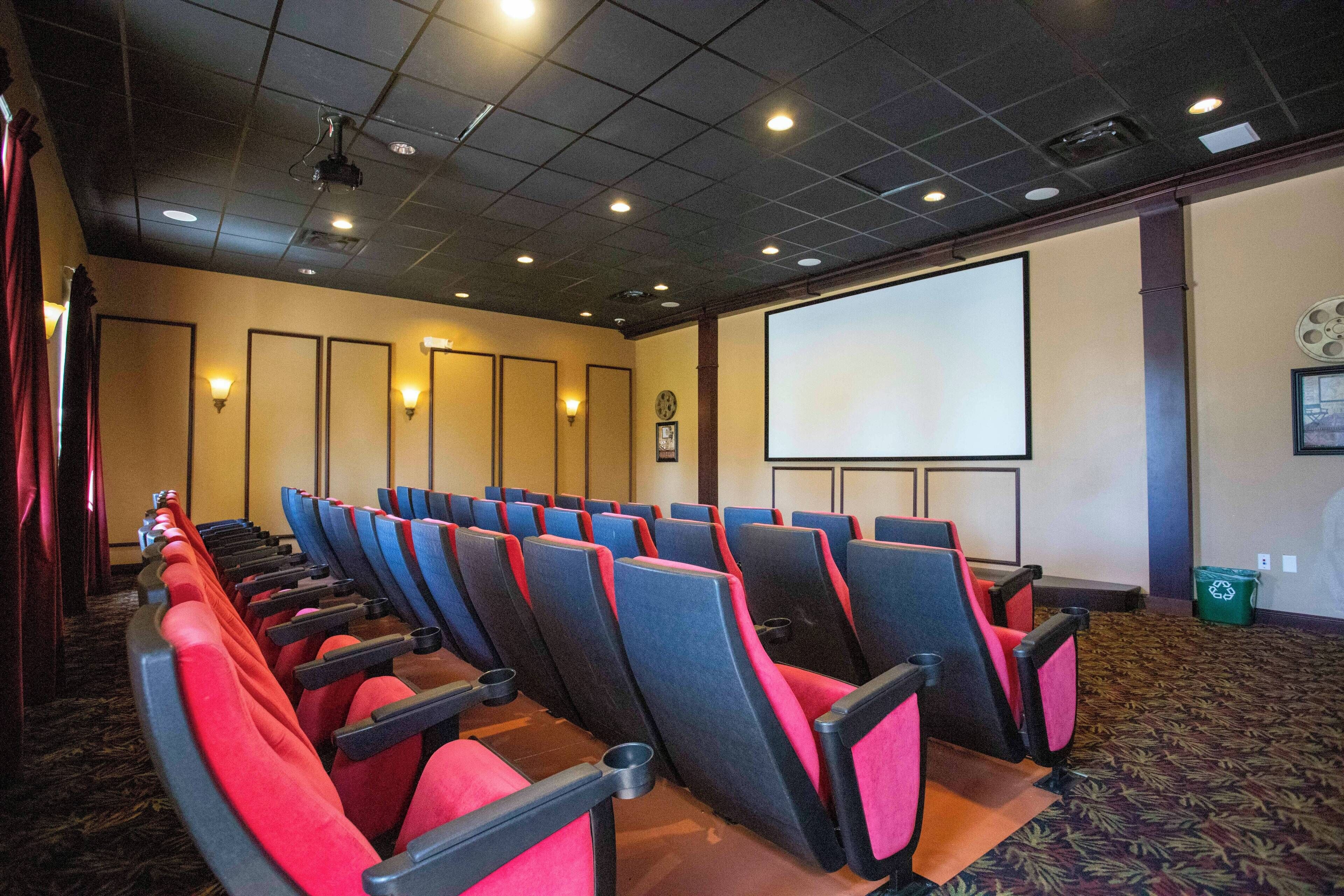 Ein Theater mit Reihen aus roten und schwarzen Sitzen, einer großen Leinwand und einem Teppichboden.