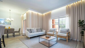 Een moderne woonkamer met een bank, twee fauteuils, een salontafel en een eethoek met een tafel en stoelen.