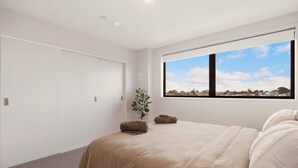 A bedroom with a large bed, a window with a view, and a door. - Waihi Beach Oasis (#B1) (Waihi Beach)