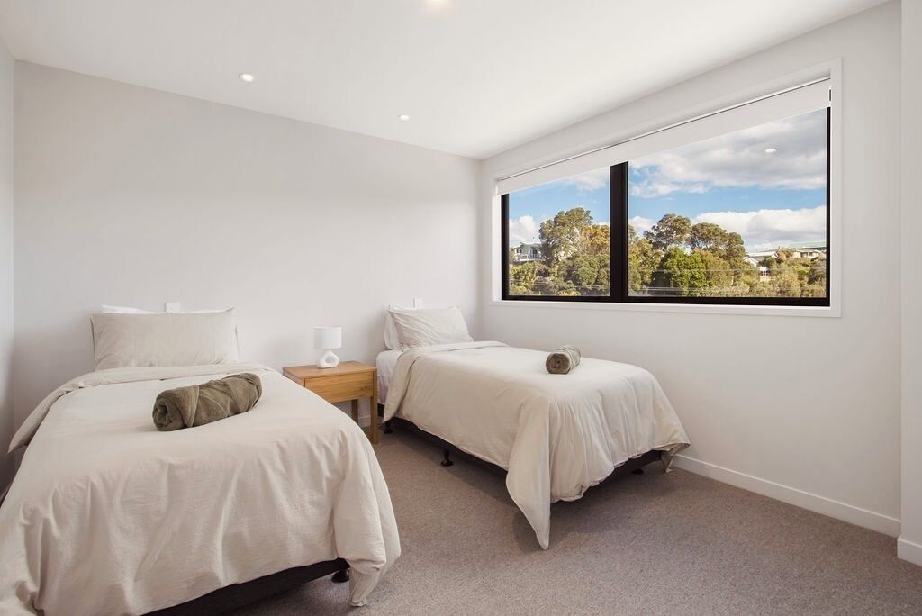 A bedroom with two beds, a window with a view, and a nightstand with a lamp.
