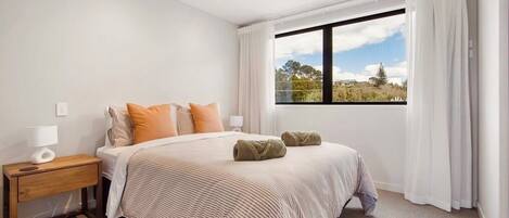 A bedroom with a bed, nightstand, and window with curtains.
