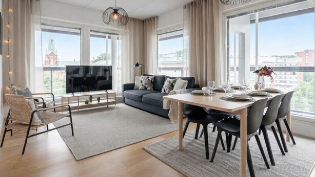 Een moderne woonkamer met een bank, televisie, eettafel en grote ramen met uitzicht op de stad.