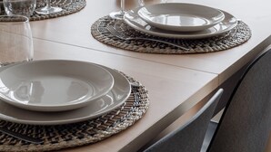 Een eettafel gedekt met borden, glazen en een vaas met bloemen.