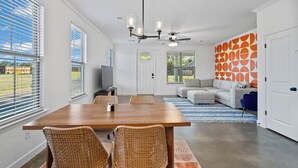 Un vaste espace de vie comprenant une table à manger, des chaises en osier, un ventilateur de plafond et un mur décoré de motifs.