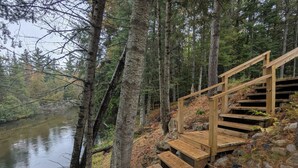 Un escalier en bois qui descend vers une rivière, entouré d’arbres.