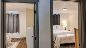 A hotel room with a bed, a nightstand, a lamp, and a window with curtains. - Greenleaf-Summer in the U.P. • Minutes to Hancock Beach & Trails (Hancock)