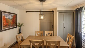 A dining area with a wooden table and chairs, a hanging light fixture, a framed picture on the wall, and a door in the background. - Greenleaf-Summer in the U.P. • Minutes to Hancock Beach & Trails (Hancock)