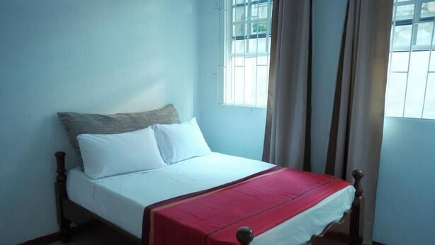 Een eenpersoonsbed met houten frame, wit beddengoed en een rode deken.