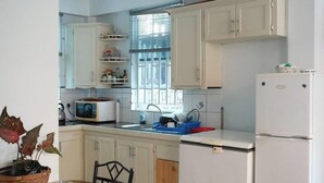 Een kleine keuken met witte kastjes, een magnetron, een spoelbak en een koelkast.