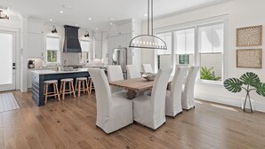 Una cocina moderna con armarios blancos, una isla central con taburetes y un comedor con sillas blancas.