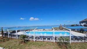 En pool med solstolar, ett inhägnat område och utsikt över havet.