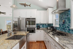 A modern kitchen with white cabinets, stainless steel appliances, a granite countertop, and blue mosaic backsplash.