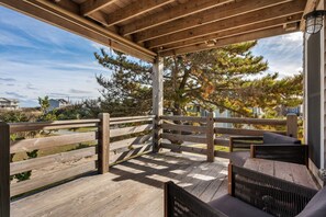 A wooden deck with a pergola, outdoor seating, and a view of trees and buildings.