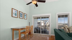 A room with a wooden table and chairs, a green sofa, and a large sliding glass door leading to a balcony.
