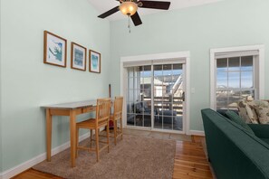 A room with a wooden table and chairs, a green sofa, and a large sliding glass door leading to a balcony.