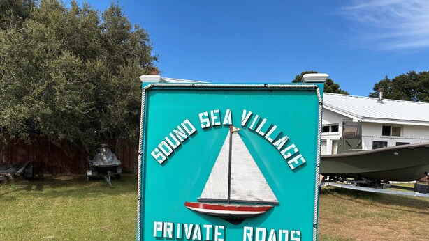 A sign for Sound Sea Village with a sailboat graphic and text indicating private roads.