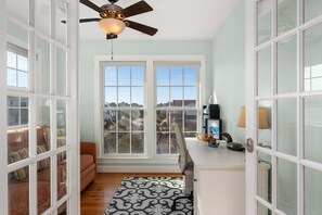 A room with a ceiling fan, a window with a view, a sofa, a desk, and a patterned rug.