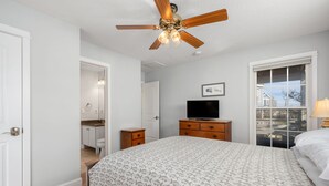 A bedroom with a bed, a ceiling fan, a television, a dresser, and a window with a view.
