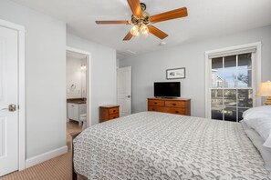 A bedroom with a bed, a ceiling fan, a television, a dresser, and a window with a view.