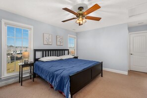 A bedroom with a bed, a ceiling fan, and a window with a view.