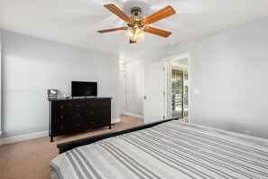 A bedroom with a bed, a ceiling fan, a dresser, and a television.