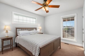 Ein Schlafzimmer mit einem hölzernen Bett, zwei Nachttischlampen, einem Deckenventilator und einem großen Fenster mit Jalousien.