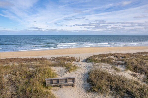 A beach with a wooden walkway leading to the shore, surrounded by dunes and vegetation.