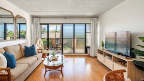 A spacious living room with a sofa, chairs, a coffee table, a TV, and a sliding glass door leading to a balcony.