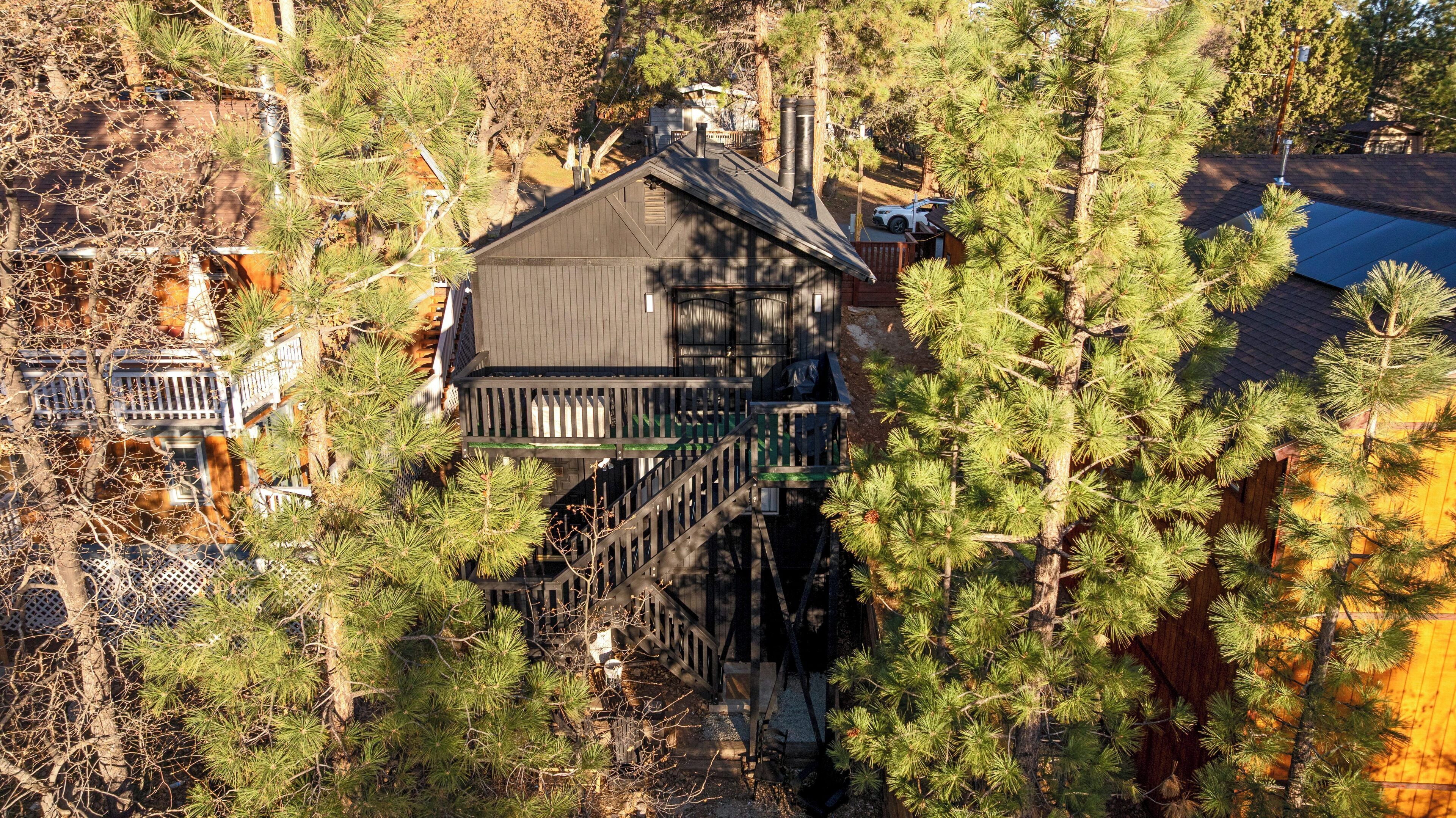 A two-story house with a deck and a chimney, surrounded by dense pine trees.