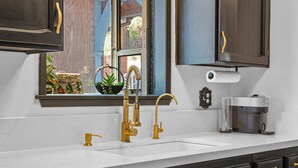 A kitchen with a white countertop, gold faucets, and black cabinets.