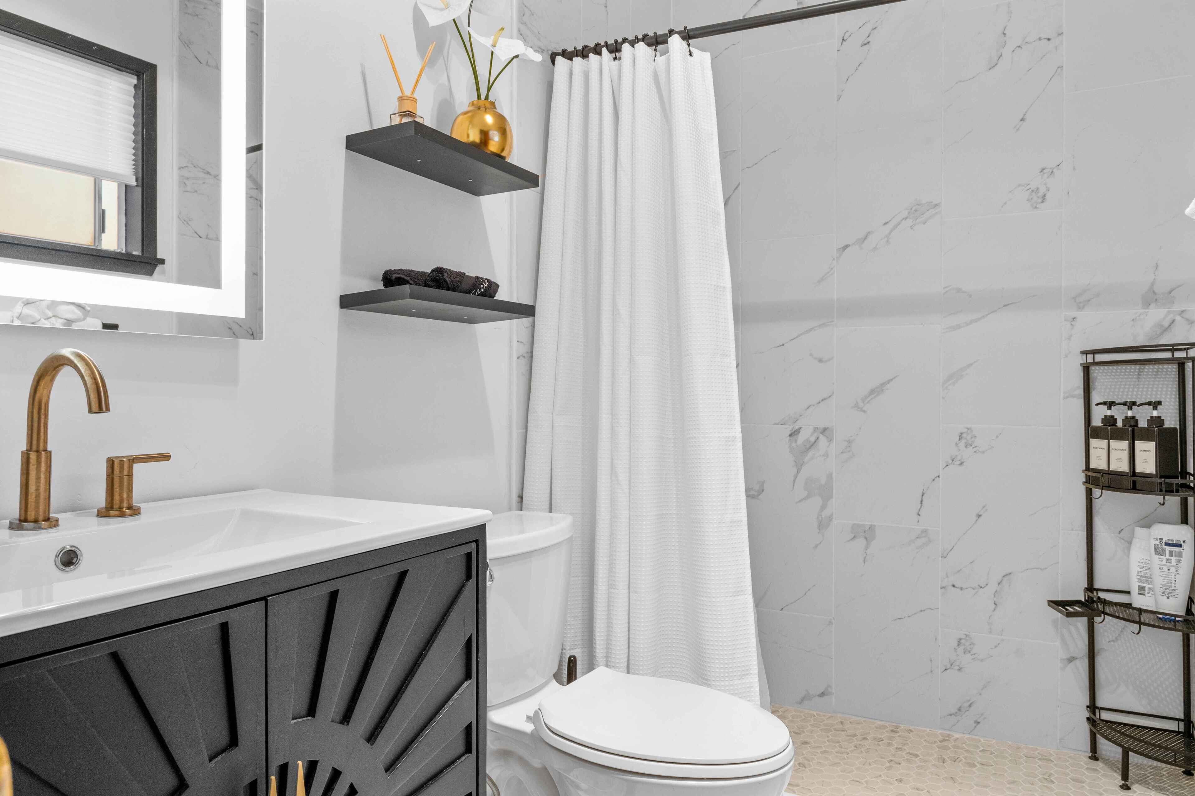 Een moderne badkamer met een witte wastafel, een zwart aanrecht en een toilet. Boven de wastafel zijn planken en er hangt een douchegordijn.
