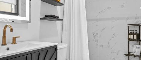 Een moderne badkamer met een witte wastafel, een zwart aanrecht en een toilet. Boven de wastafel zijn planken en er hangt een douchegordijn.