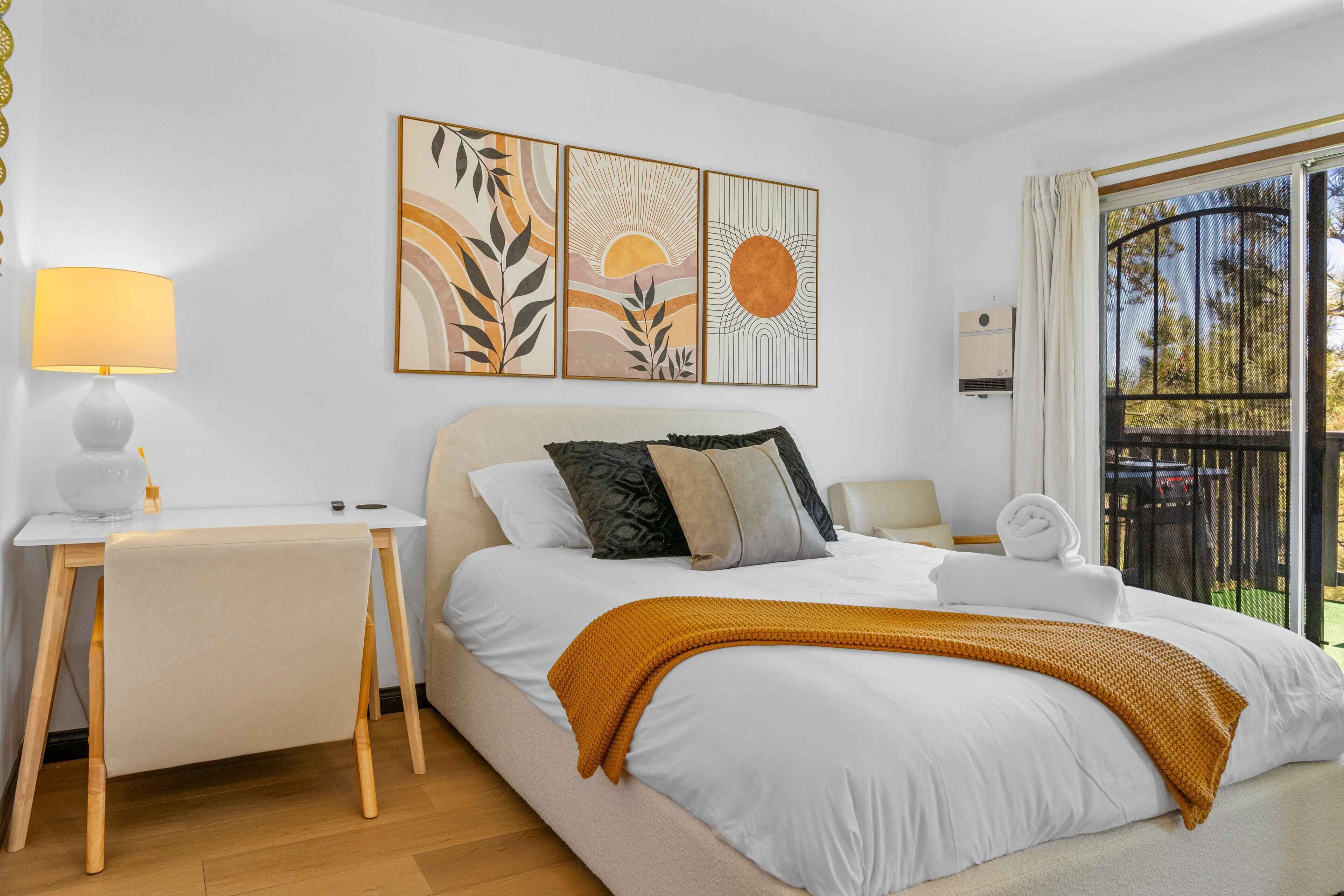 A bedroom with a bed, a bedside table, a lamp, and artwork on the wall.