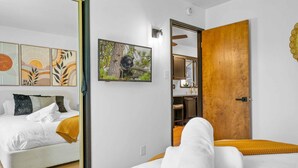 A modern bedroom with a bed, a painting, and a wooden door leading to a bathroom.