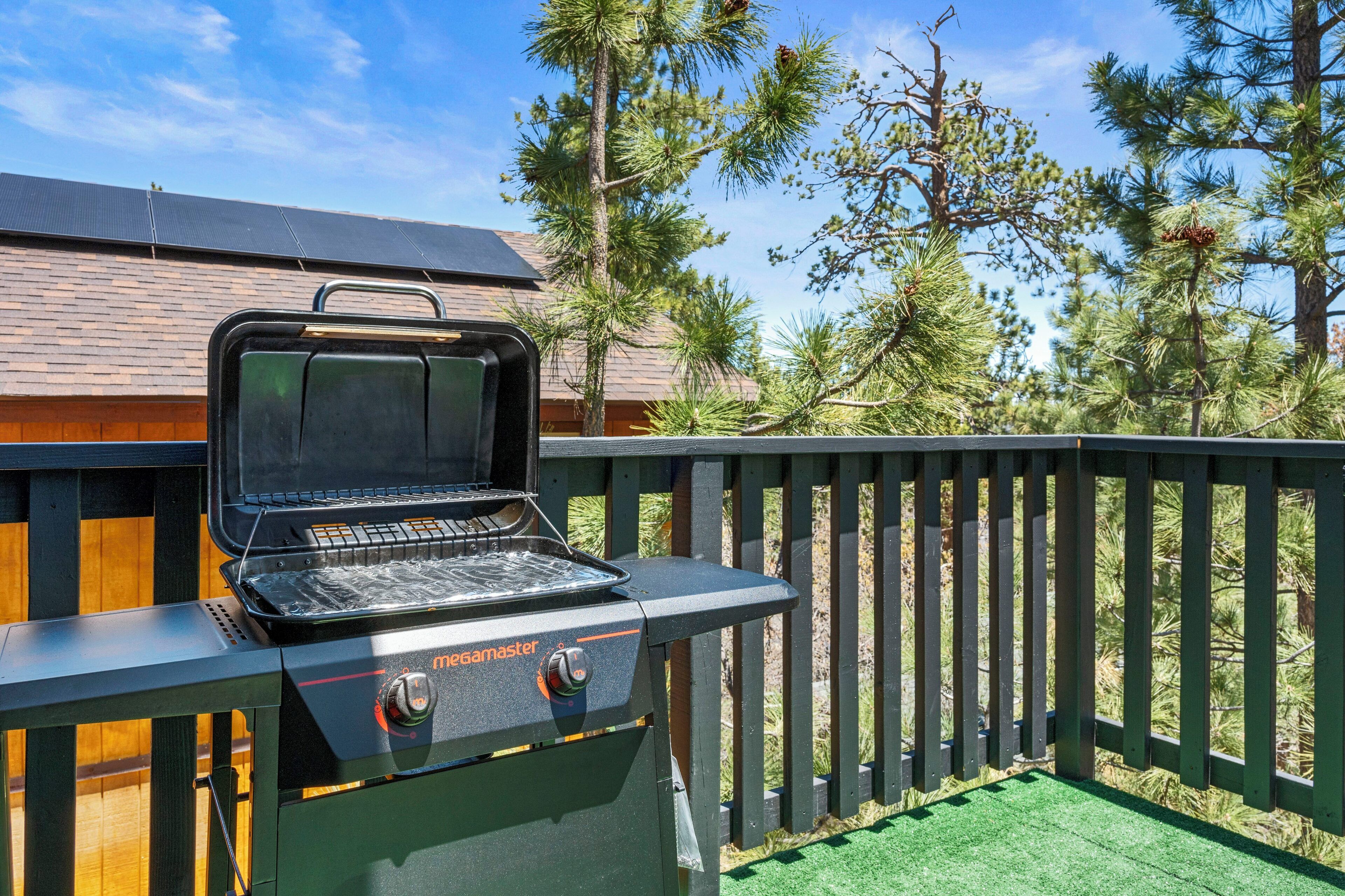 A portable outdoor grill with a digital display, set against a backdrop of a wooden deck and a house with a sloped roof.