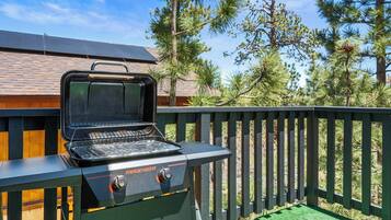 A portable outdoor grill with a digital display, set against a backdrop of a wooden deck and a house with a sloped roof.