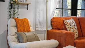 A living room with a sofa and armchair, a floor lamp, and a hanging plant.