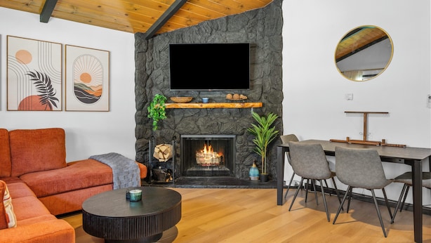 A modern living room with a fireplace, a flat-screen TV, a dining area with chairs, and artwork on the wall.